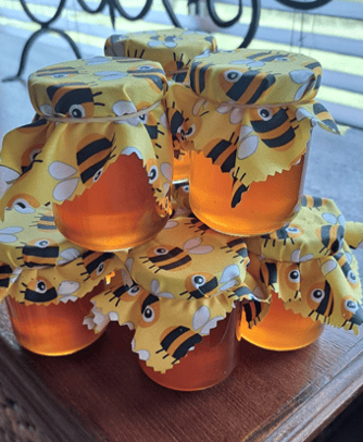 Handcrafted raw honey jars in pyramid stack with yellow bee motif lids on a display