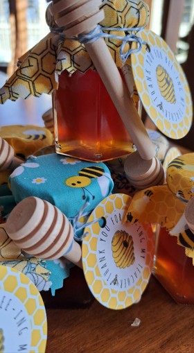 Bee-themed honey jar arrangement with wooden dippers and bee-pictured cloth lids on rustic wooden table and glass window on the background