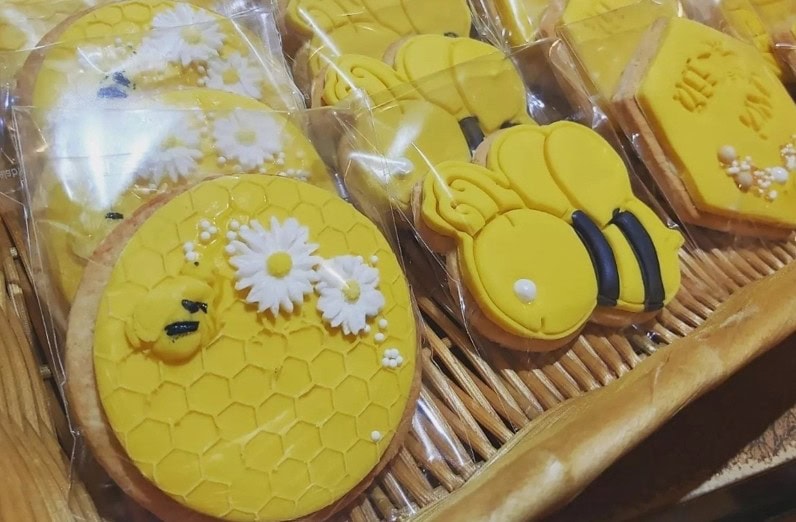 Wicker basket filled with individually wrapped bee-themed honey cookies decorated with yellow icing, honeycomb patterns, daisies, and cartoon bees, perfect for a honey-inspired celebration